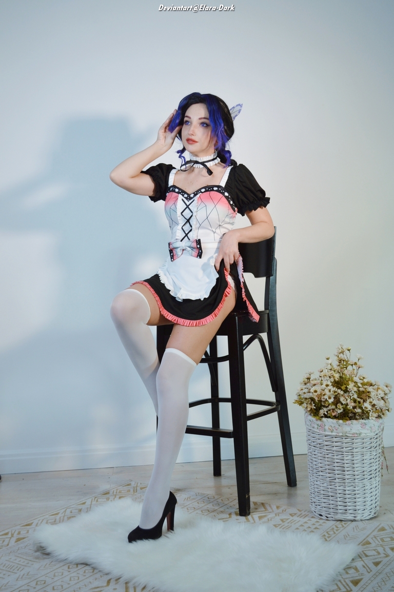 A person dressed in a nostalgic outfit with a corset-style top and a frilly skirt, sitting on a bar stool. They have blue hair with purple highlights, wearing knee-high stockings and high heels, against a minimalistic background with a potted flower arrangement.