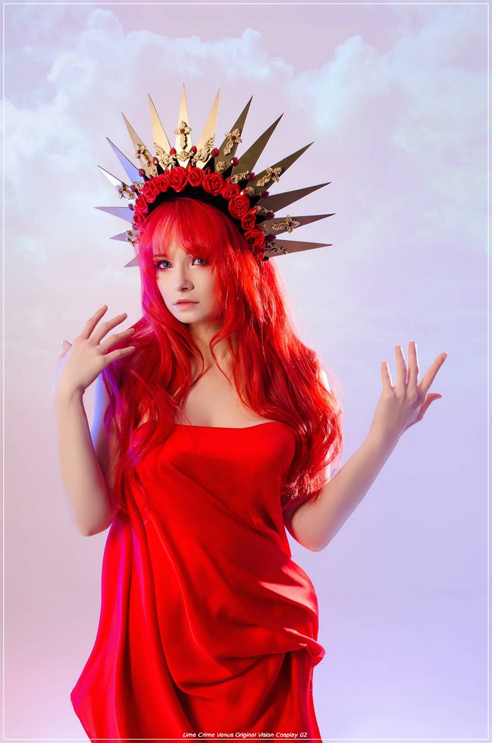 A person with long red hair and a crown adorned with roses and spikes, wearing a flowing red dress, posing against a soft, pastel background.