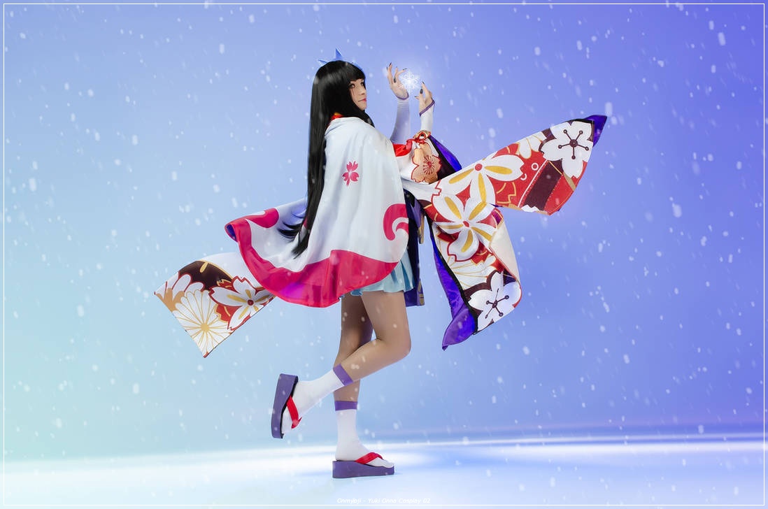A person in a colorful kimono with long black hair, standing gracefully in a snow-like setting, holding a shimmering object in one hand.