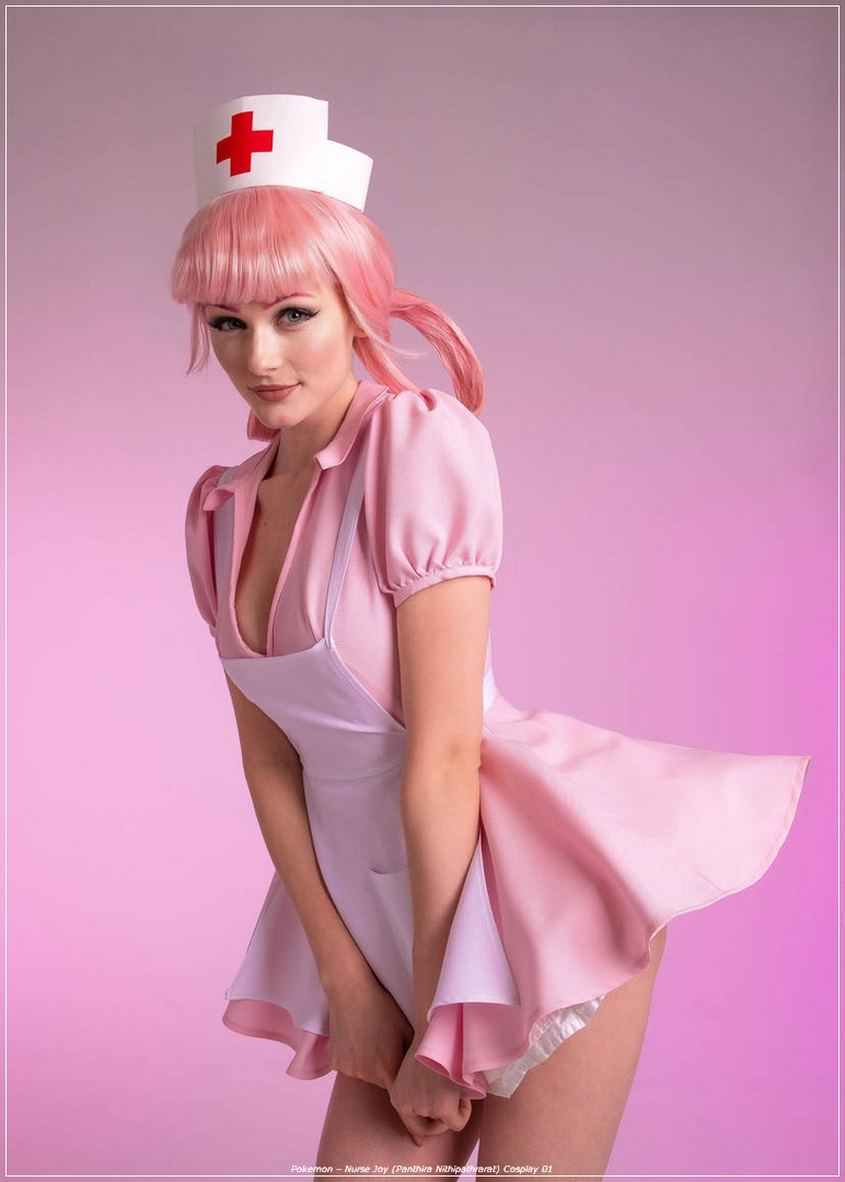 A person dressed as a nurse, wearing a pink costume and a nurse's cap, posing playfully against a soft pink background.