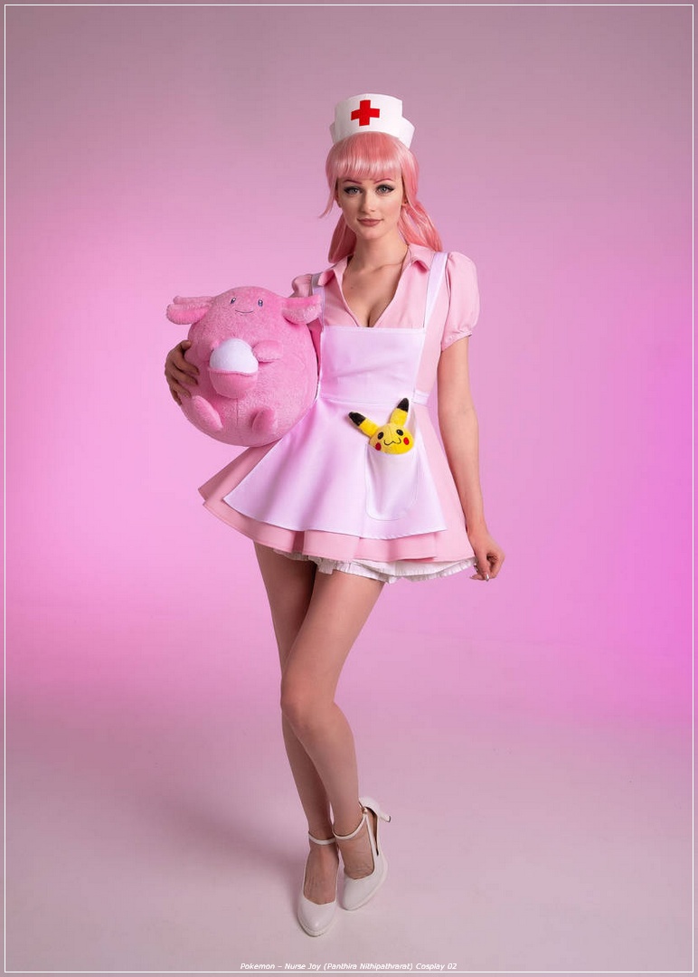 A person dressed as Nurse Joy from Pokémon, featuring pink hair and a pink nurse outfit, holding a plush toy in one arm and displaying a Pikachu plush in their apron pocket, set against a soft pink background.