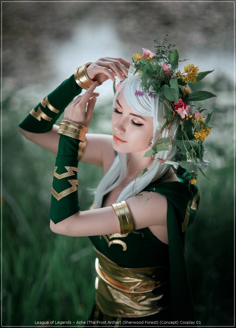 A female cosplayer dressed as Ashe from League of Legends, wearing a green costume adorned with gold accents and a floral crown, poses gracefully in a natural setting.