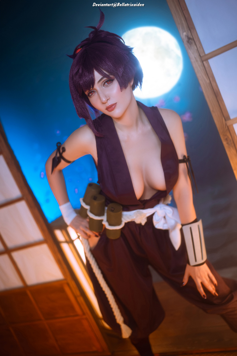 A person in a dark outfit poses confidently in front of a wooden backdrop with a blue light and a full moon visible.