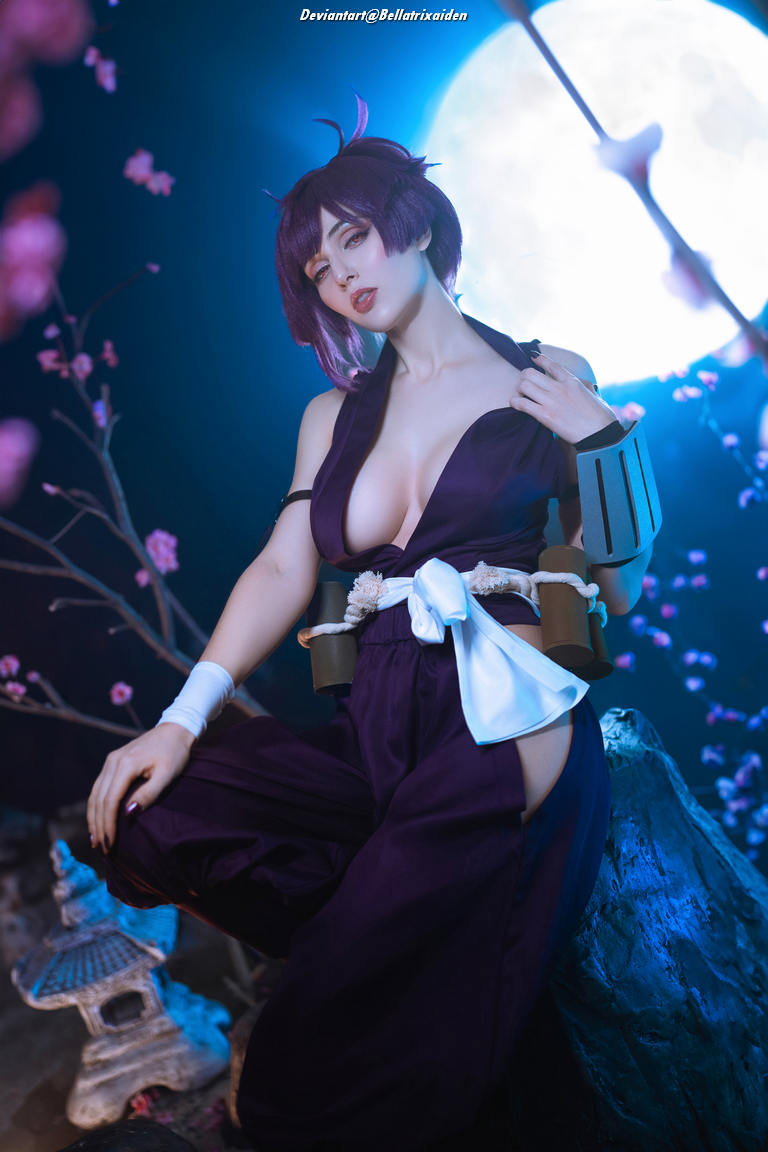 A person dressed in a dark purple outfit with a white sash, posing in a mystical setting lit by blue and moonlight, surrounded by delicate pink flowers.