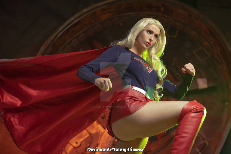 A cosplayer dressed as a superhero with long blonde hair and a red cape, striking a powerful pose.