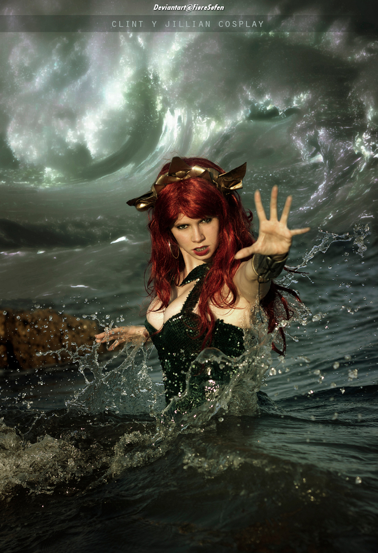 A person in a green costume with long red hair stands in water, reaching out with one hand as waves crash around them, capturing an intense and dramatic pose.