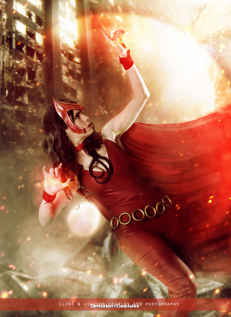 A female cosplayer in a red costume and cape, striking a dynamic pose and casting magical energy with her hands, set against a dramatic, fiery background.