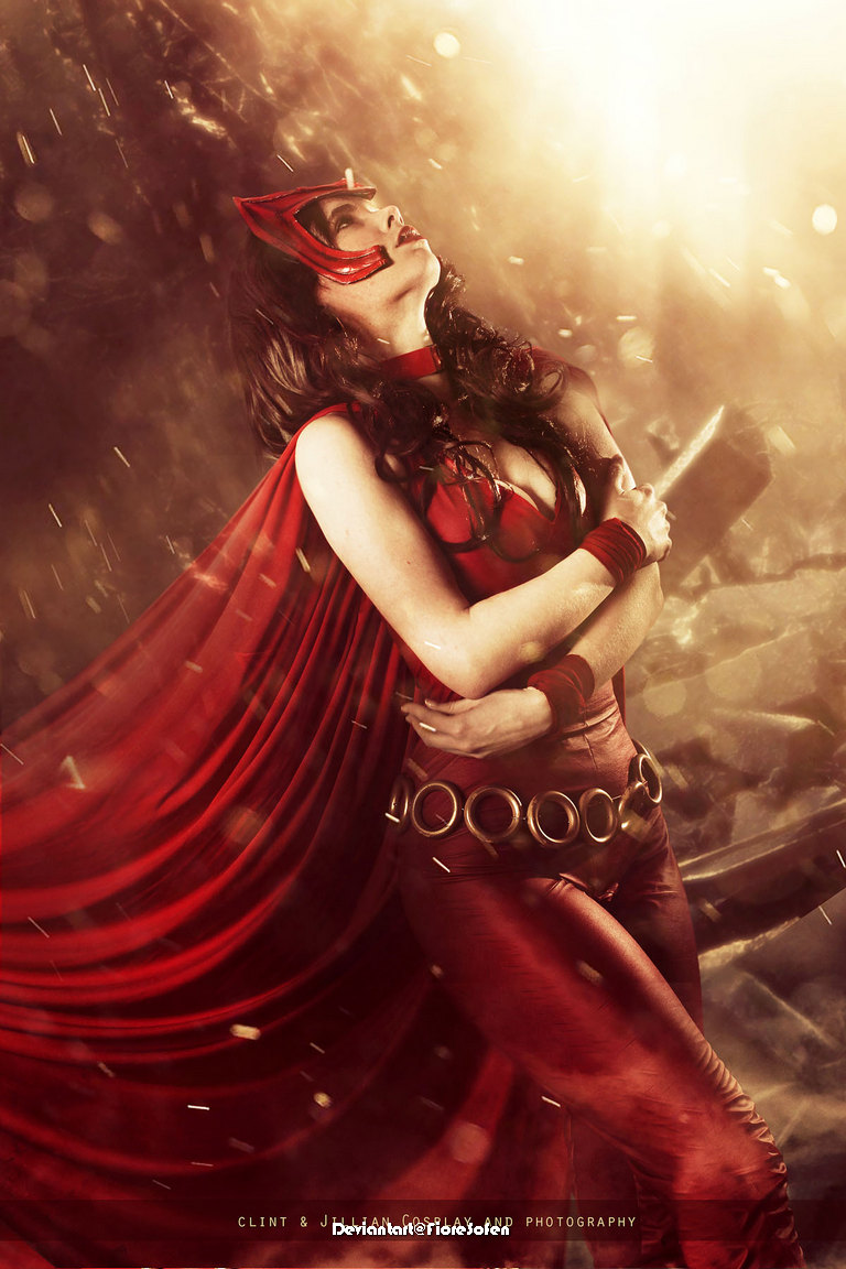 A woman dressed in a red superhero costume with a flowing cape, striking a dramatic pose against a glowing background.