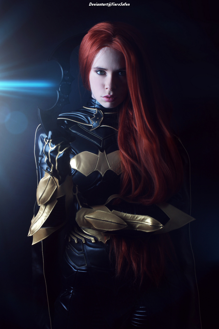 A person with long red hair wearing a sleek black and gold costume resembling a superhero outfit, posing confidently against a dark background with a dramatic blue light effect.