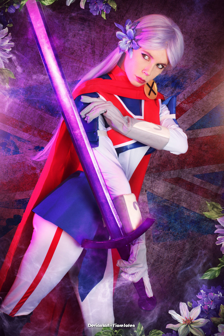 A female cosplayer dressed as a character with purple hair, wearing a costume featuring the Union Jack, holding a purple sword, with flowers in her hair and a dramatic background.