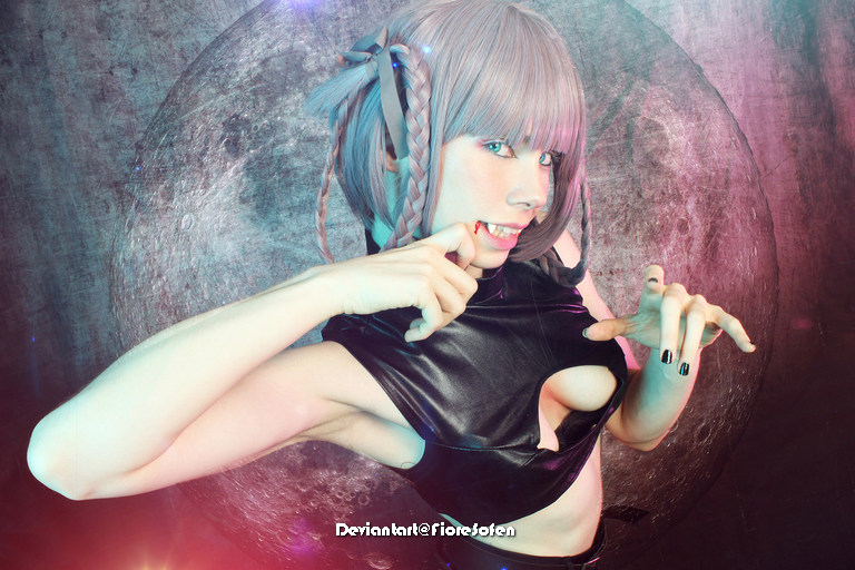 A person with short grey hair wearing a black sleeveless outfit poses dramatically against a colorful backdrop featuring a large moon.