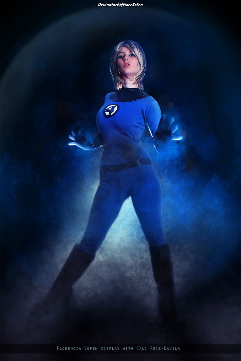 A female cosplayer dressed as a superhero character from the Fantastic Four, featuring a blue costume and the number four emblem, posed against a dark, misty background.