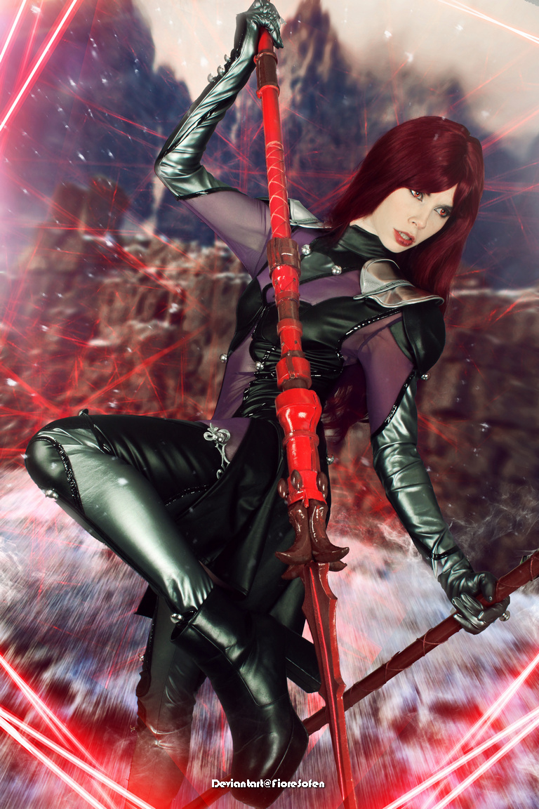 A person in a dark, stylized costume holds a red staff, posed dramatically against a colorful, abstract background.