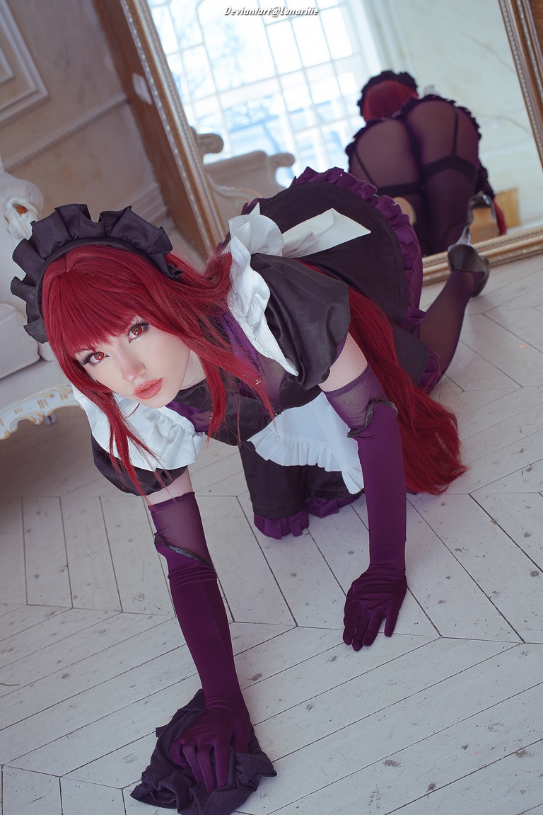 A woman in a maid costume with long red hair poses on the floor, looking at the camera with a mirror reflecting her back.