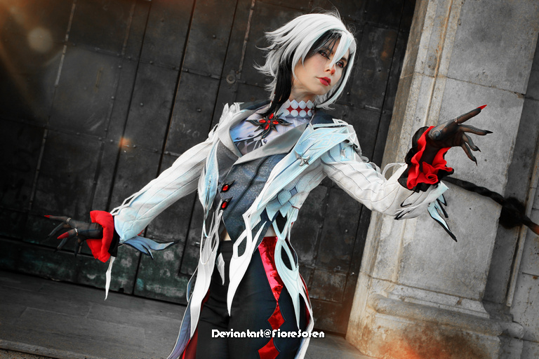 Person in elaborate fantasy costume with white hair and striking makeup, posing dramatically against a textured background.