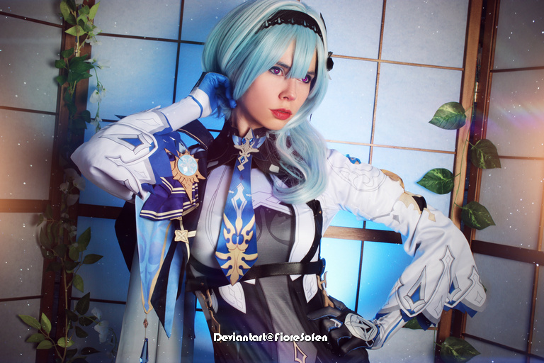 A person in a stylish fantasy costume with blue hair, striking a pose against a backdrop of wooden panels and greenery.