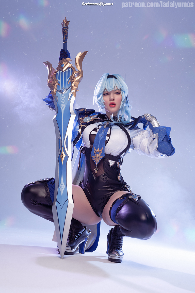 A character in a blue and black outfit poses while holding a large ornate sword, with a light background and scattered reflections.