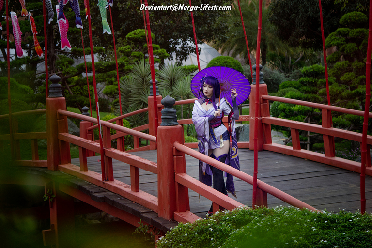 A person in traditional Japanese attire stands on a wooden bridge, holding a purple parasol, surrounded by lush greenery.