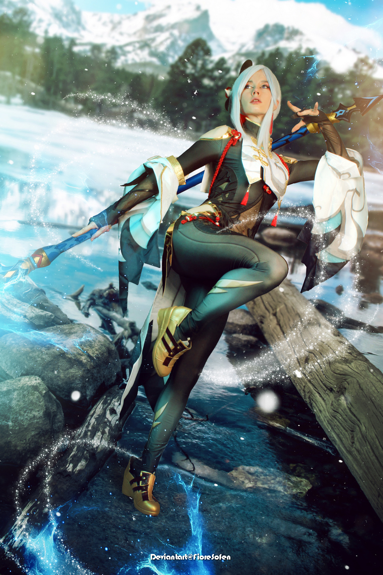 A character with long hair and a stylized outfit poses dramatically in a snowy landscape, holding a spear and surrounded by swirling blue energy.