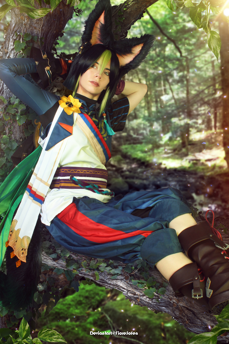 A person in a fantasy costume with pointed ears lounges on a tree branch, surrounded by greenery and soft lighting.