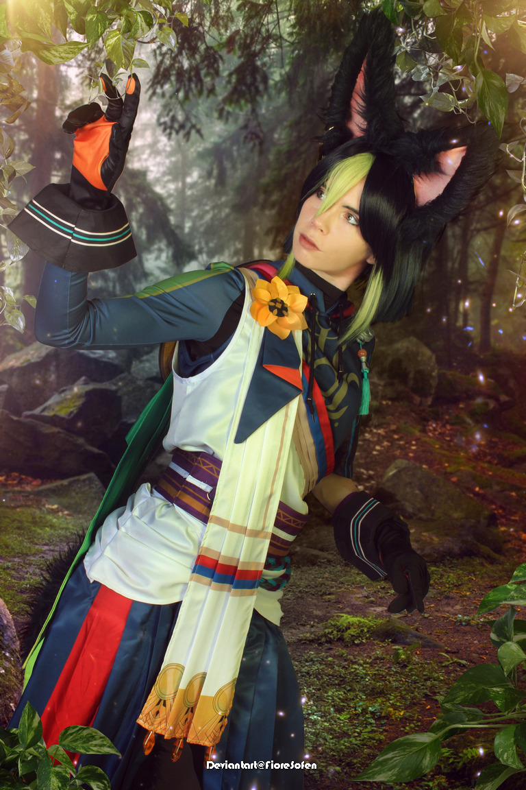 A person in a colorful costume inspired by a mythical character, posing in a forest setting with a backdrop of greenery and rocks.