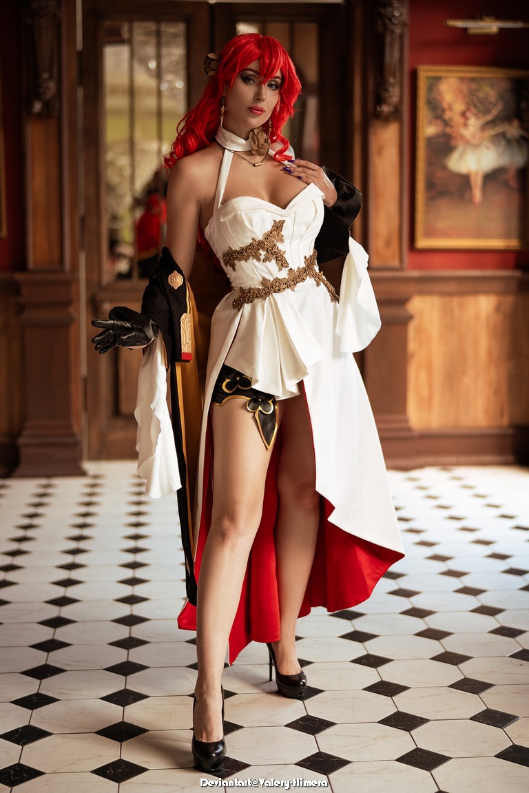 A woman in a striking costume with red hair, featuring a white dress with gold accents and a black cape, posing in an elegant indoor setting with a checkered floor.