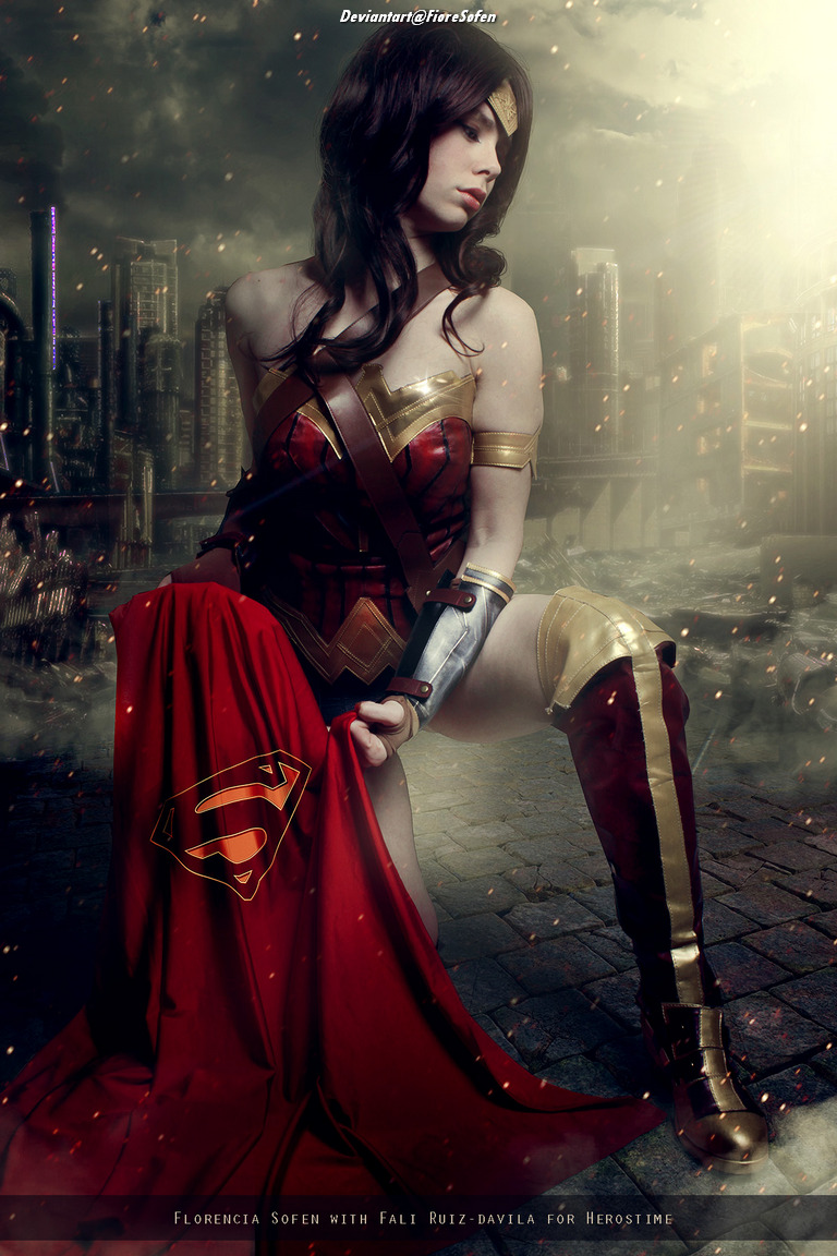 A female figure in a superhero costume, featuring a red dress with a Superman logo and gold accents, posed in a dramatic setting with a cityscape in the background.