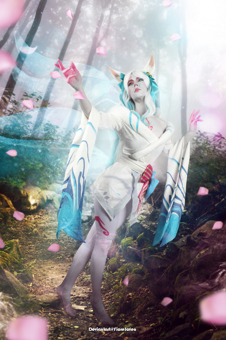 A beautifully costumed figure with fox-like features poses in an ethereal forest, surrounded by pink petals and soft light, conveying a mystical atmosphere.