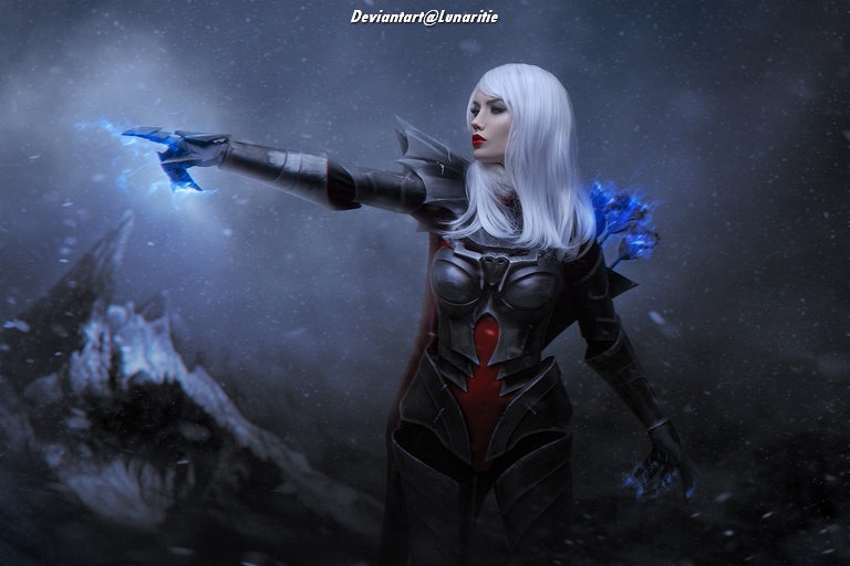 A female character with long white hair wearing dark, armored clothing and wielding blue magical energy, standing against a dark and misty background.