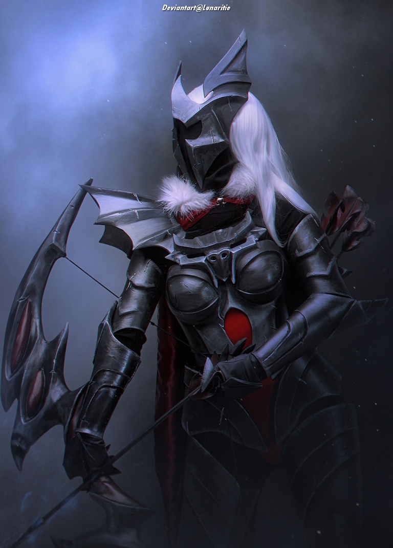 A female warrior in dark armor with a menacing helmet, wielding a weapon and standing against a misty background.