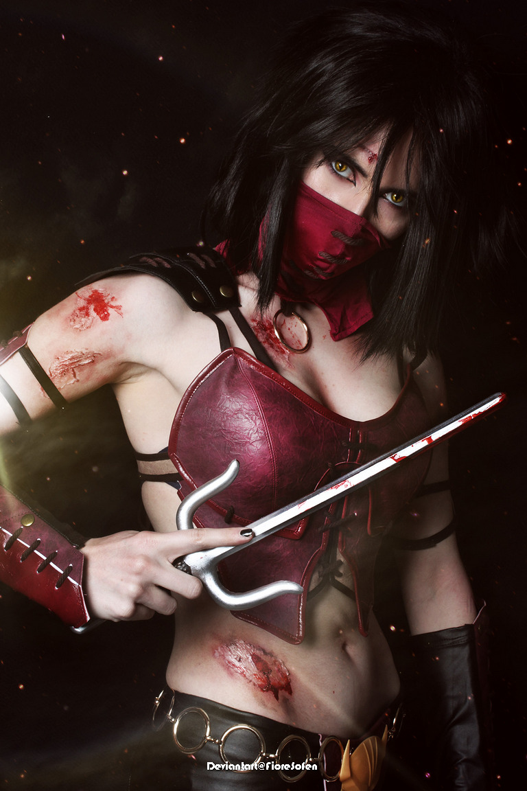 A fierce cosplayer dressed in a red and black outfit with a mask, holding a bloody weapon, showcasing battle scars on their body, exuding a bold presence.