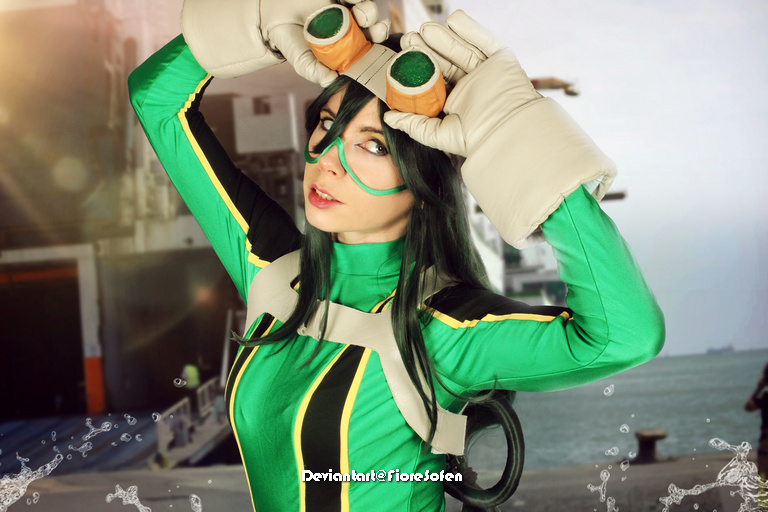 A person dressed in a green costume with large gloves and goggles, posing playfully against a maritime background.
