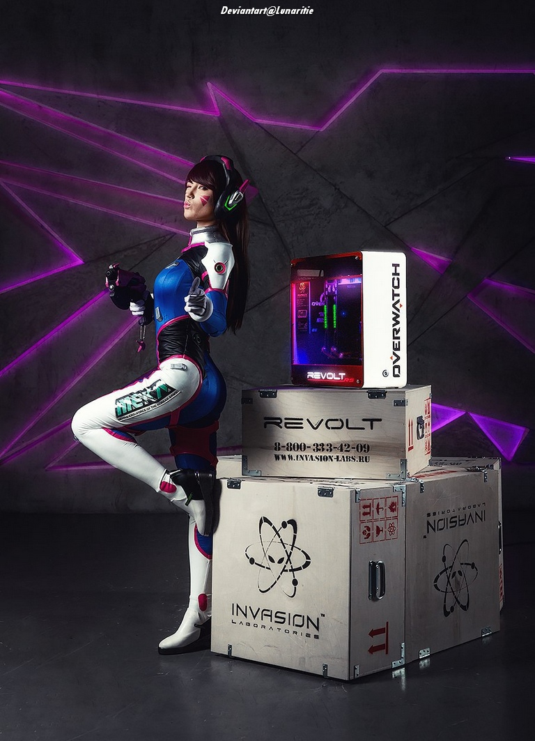 A woman in a futuristic cosplay outfit stands next to gaming-themed crates and a custom computer, exuding a confident gaming persona against a dark, neon-lit backdrop.
