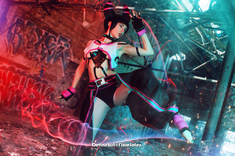 A dancer in a dramatic pose wearing a stylish outfit with pink and black accents, set against a graffiti-covered industrial background.