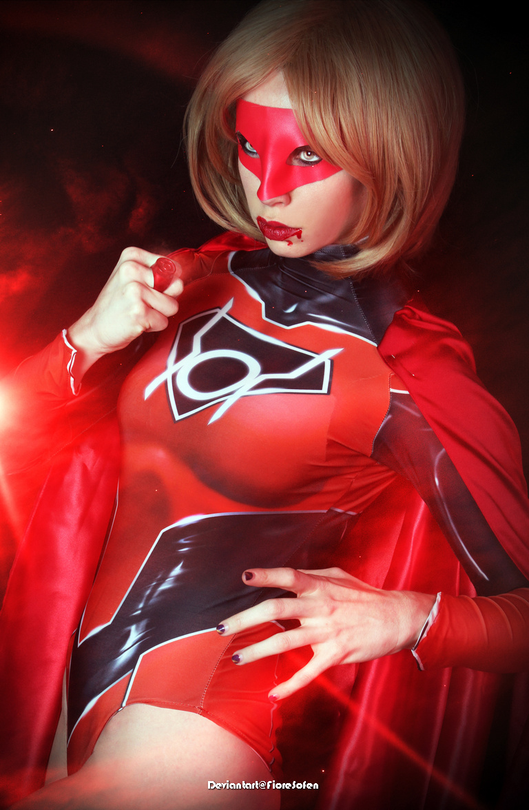 A person dressed in a red and black superhero costume with a cape, striking a confident pose and looking directly at the camera.