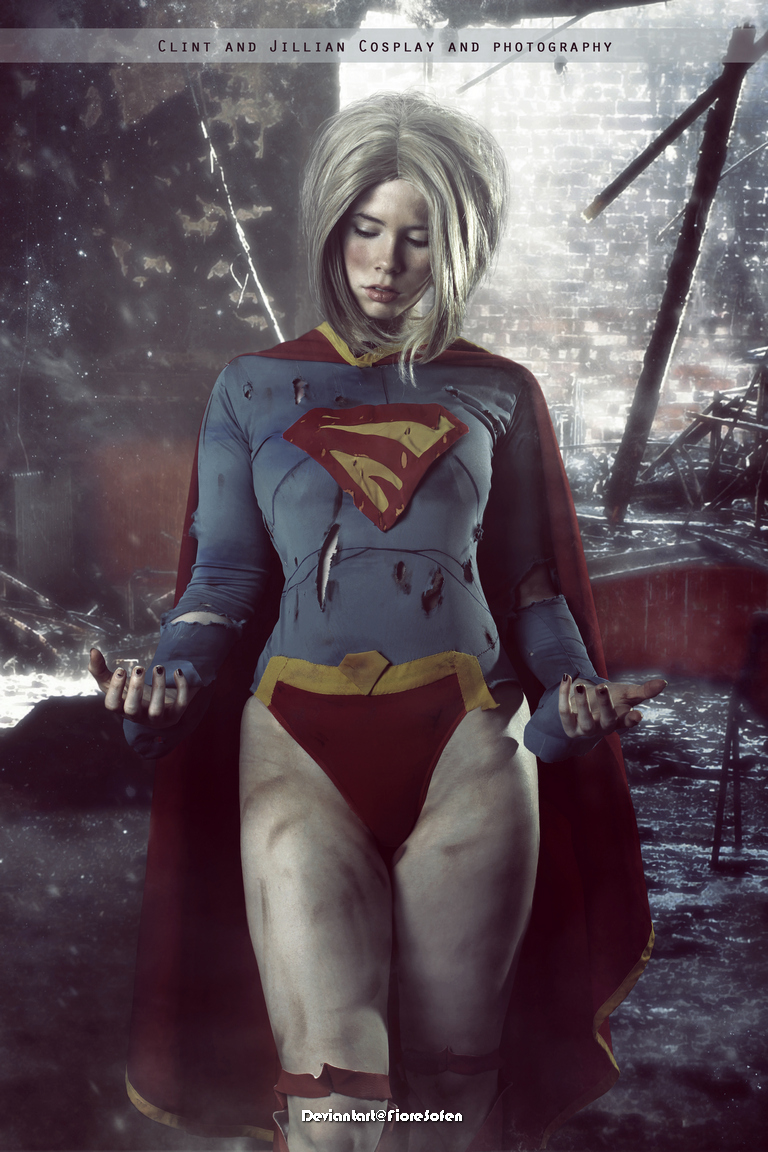 A woman cosplaying as a superhero, wearing a torn costume with a red cape and standing in a desolate, post-apocalyptic setting.