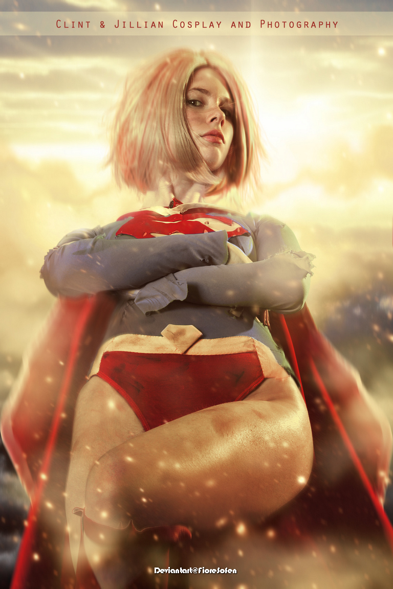 A female cosplayer dressed as a superhero, standing confidently with her arms crossed, in a dramatic, glowing background.