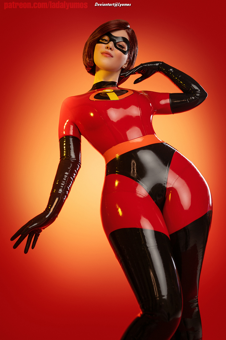 A person dressed in a shiny, red and black superhero costume with a distinctive logo, posing against a vibrant orange background.