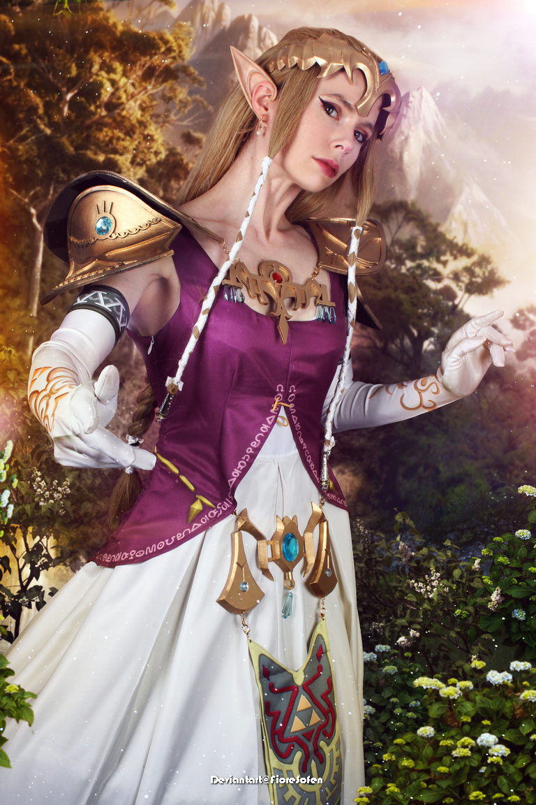 A woman dressed as Princess Zelda from a fantasy game, wearing a purple gown with gold accents and white gloves. She has long blonde hair, pointed ears, and stands in a lush, natural setting with a soft, magical glow.