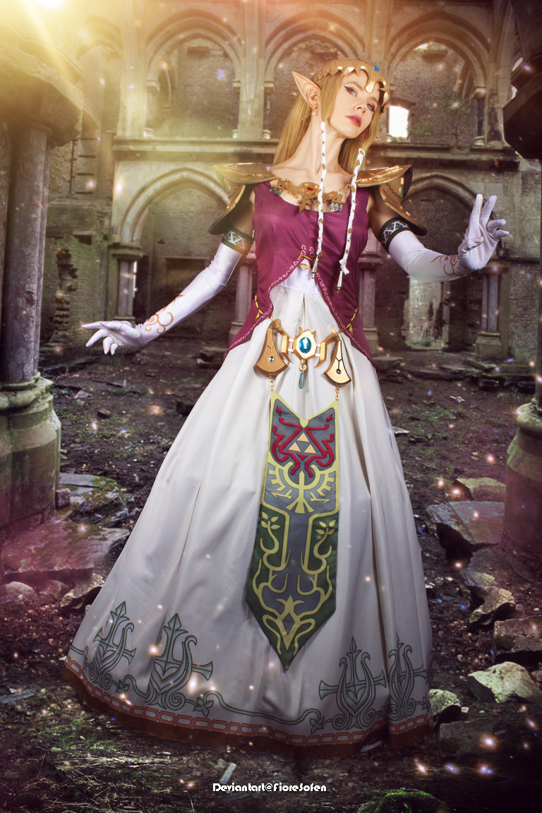 A woman dressed as a fantasy character in an ornate gown standing in a ruined castle setting, with magical lighting and an elegant pose.