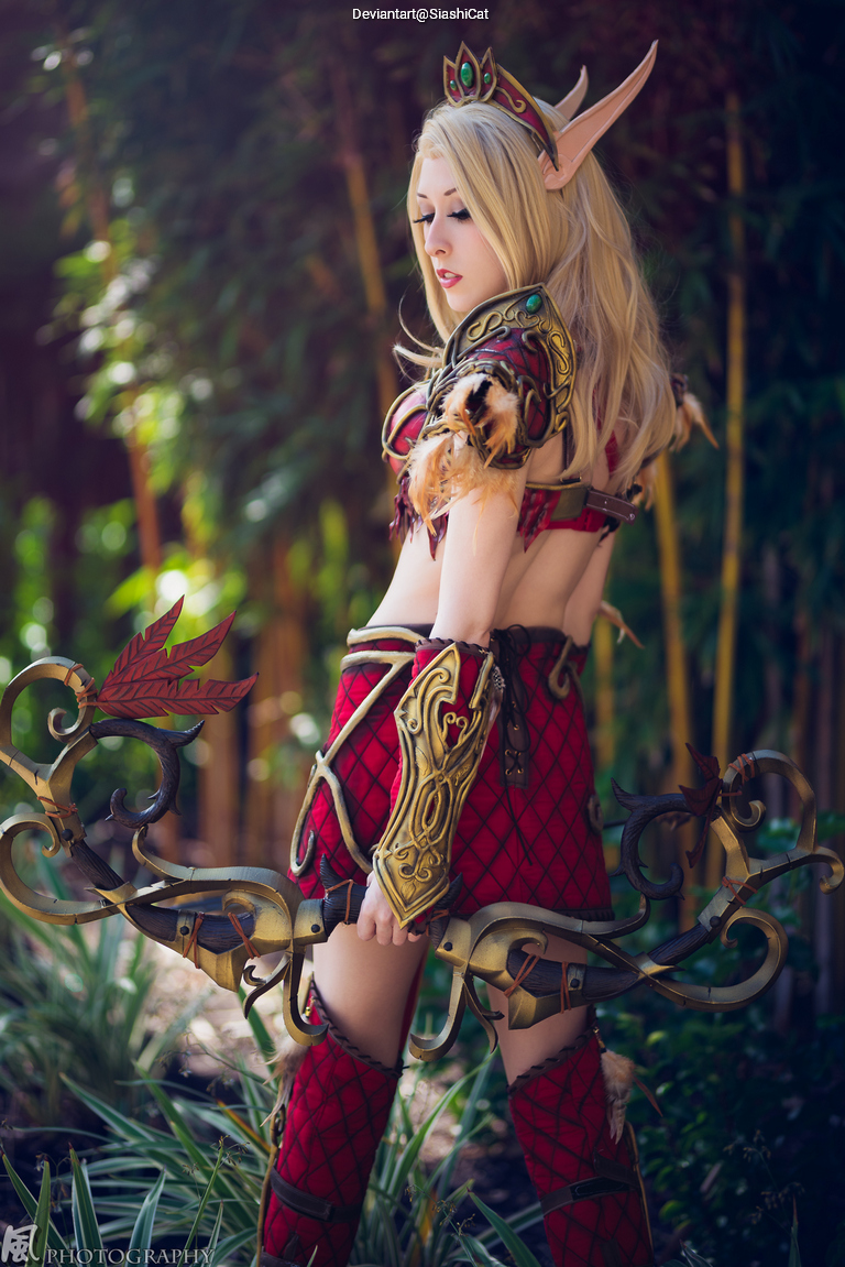 A female cosplayer in an elaborate fantasy outfit with an ornate bow, posing in a lush outdoor setting.
