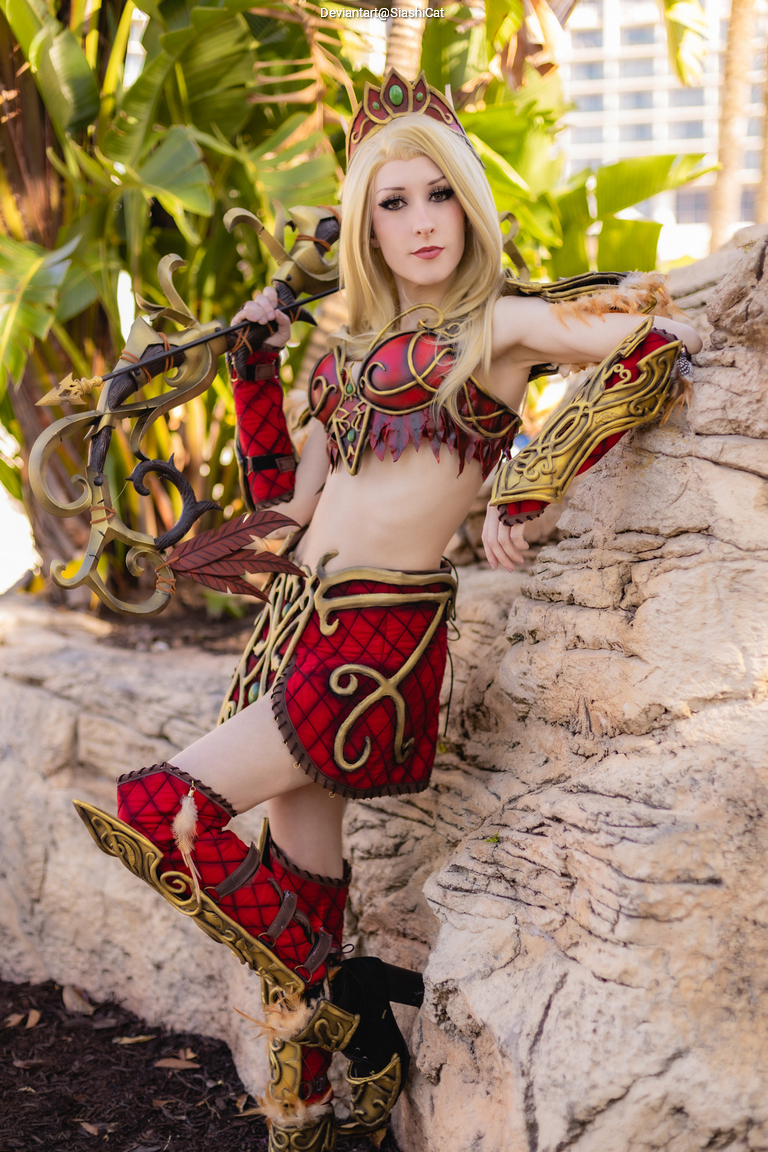 A person in a detailed red and gold fantasy-inspired costume posing against a rocky background with greenery.