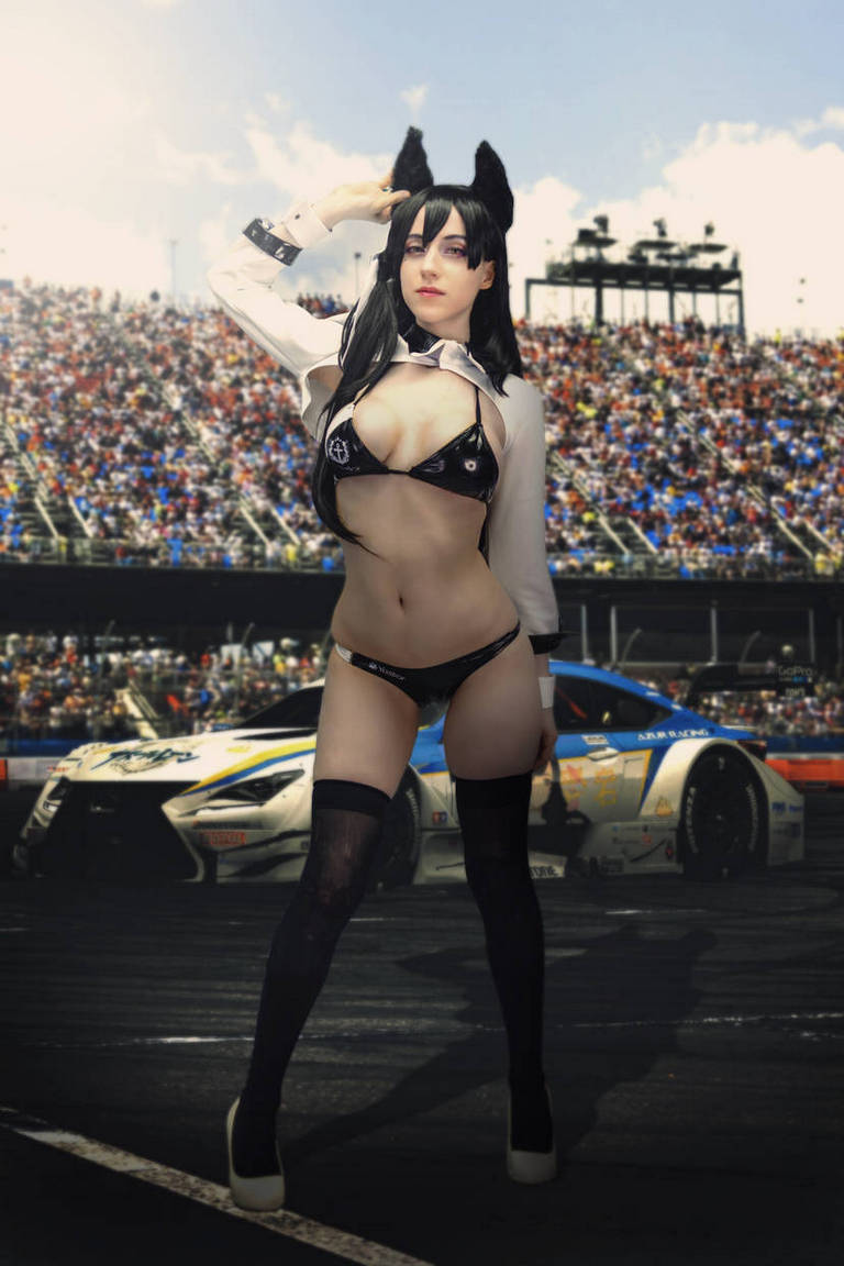 A woman in a revealing outfit with cat ears poses confidently in front of a racetrack filled with spectators and racing cars.