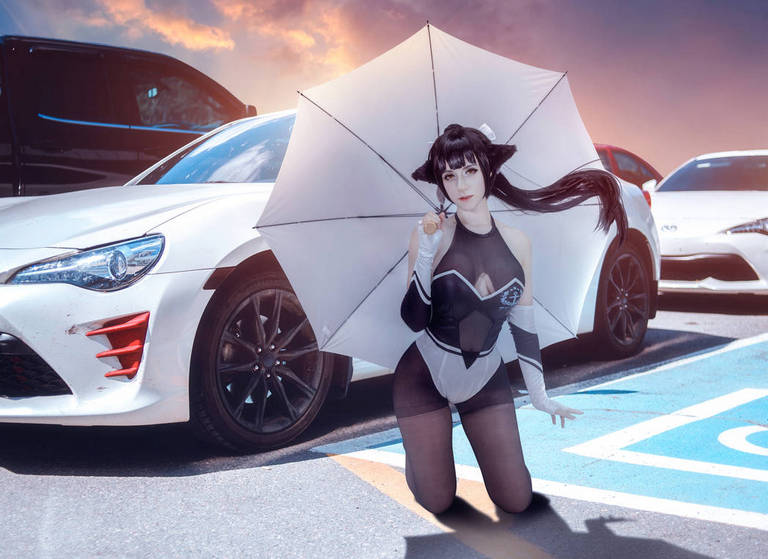 A person in a stylish outfit, kneeling on the ground with an umbrella, surrounded by parked sports cars in a colorful setting.