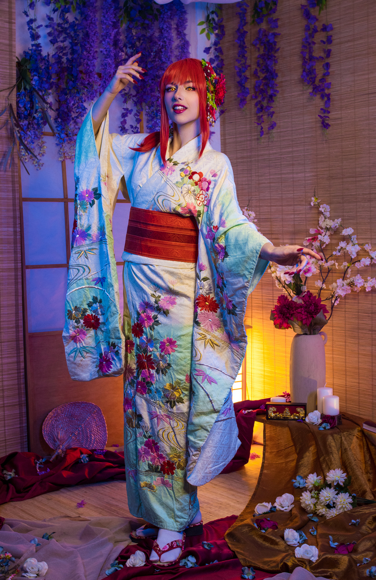 A woman in a colorful kimono poses gracefully in a themed setting adorned with flowers and candles.