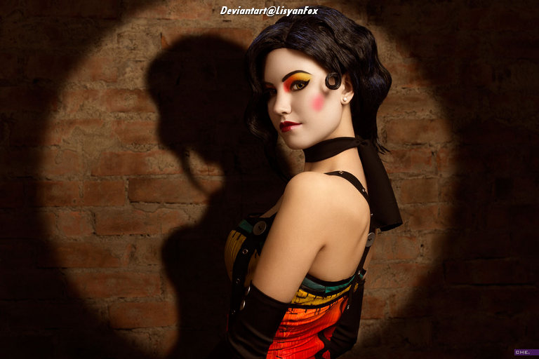 A woman with striking makeup and a colorful outfit poses against a textured brick wall, creating a dramatic shadow effect.