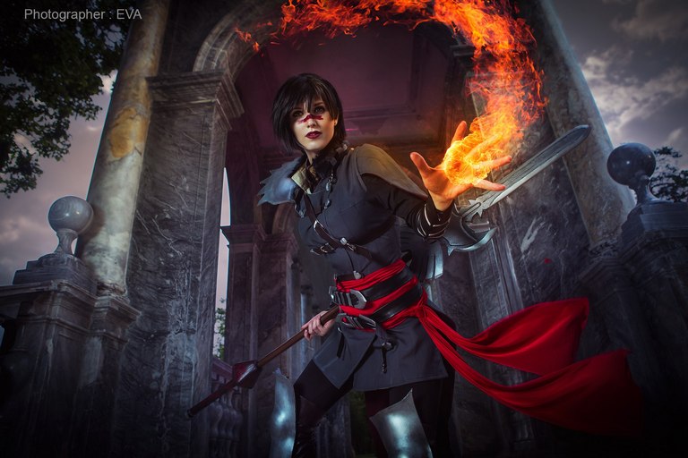 A character in a dark outfit, wielding a sword and casting fire from their hand, stands in a mysterious outdoor setting with classical architecture.