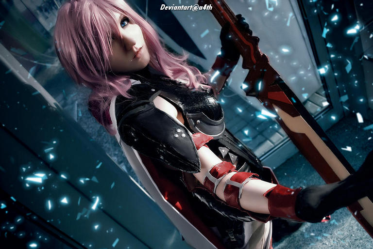 Female cosplayer with long pink hair dressed in a black and red costume, holding a weapon, posing in a futuristic setting with blue lighting effects.