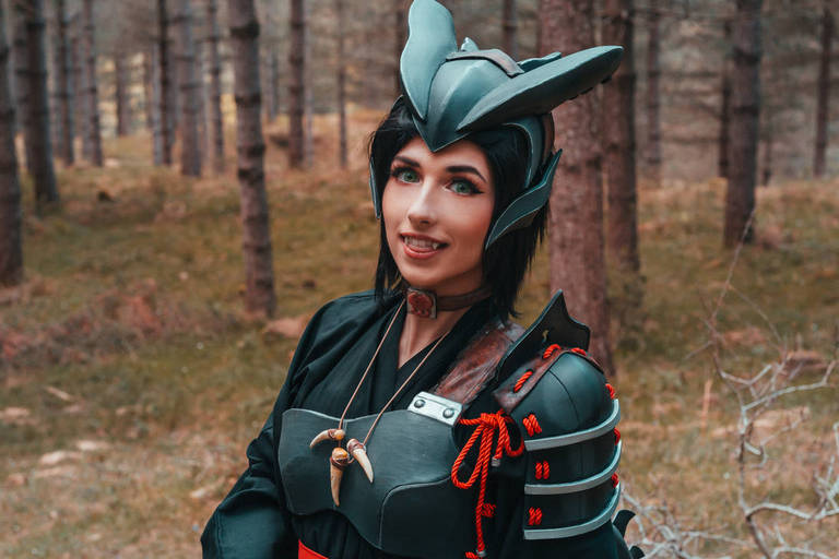Person in a dark costume with armor and headpiece, standing in a forest setting.