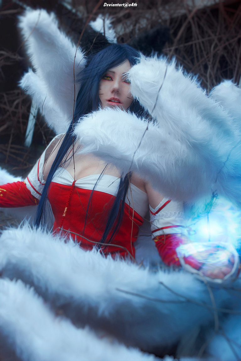 A fantasy character with long dark hair wearing a red and white outfit, surrounded by large fluffy tails and glowing blue energy, sitting in a natural environment.